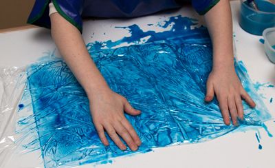 A child covers a sheet of paper with tempera paint with a piece of plastic wrap