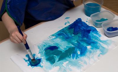 A child applies a generous amount of tempera paint on a piece of wetted paper