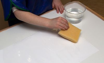 child putting water on paper with a sponge for plastic wrap art