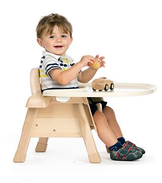 A child sits on a chair with tray and plays with a wooden car