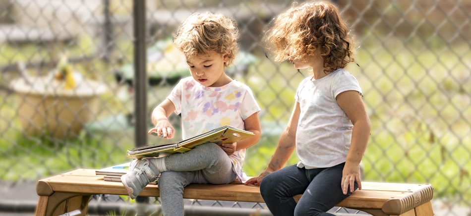 preschool girls reading a book on a bench outdoors