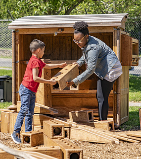 A child and teacher taking blocks out of a shed