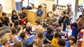 Adults and children sitting on the floor and chairs, playing musical instruments during circle time.