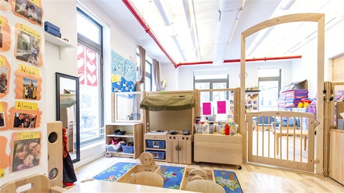 A classroom with a wooden 3-room divider, play kitchen, and a gate leading to another area.