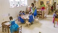 Children and teachers in a bright classroom with wooden furniture and natural light.