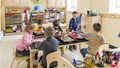 Children seated around a table, engaged in various art activities with craft supplies.