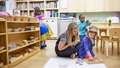 Teacher and two children playing a word game on the floor in a classroom.