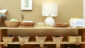 A wooden shelf with various woven baskets, a lamp, and learning materials, some labeled with words.