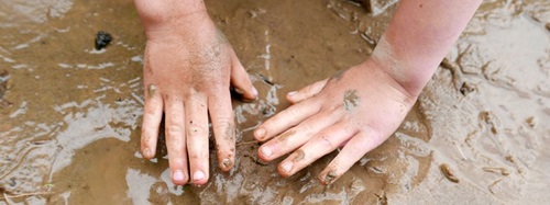 child making hand prints in the mud