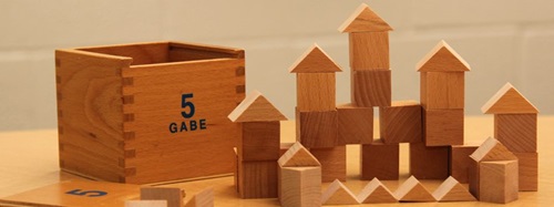 Wooden blocks from Froebel Gabe 5 set arranged to form houses and other structures.