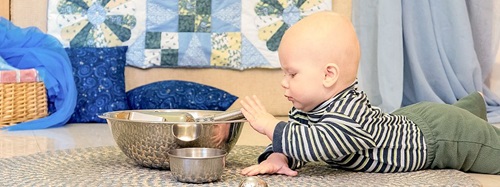 A baby playing with a metal bowl and wisk.