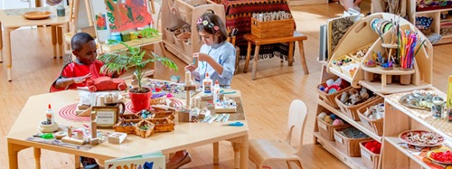 Two children engaged in creative activities at a makerspace table with various craft supplies.