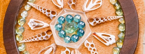A close-up of a wooden wheel with shells and glass beads arranged on a tan surface.