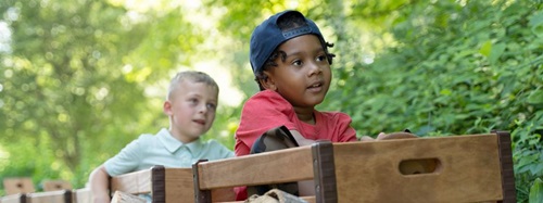 Two young boys, one in a red shirt and blue cap, the other in a light blue shirt, playing outdoors.