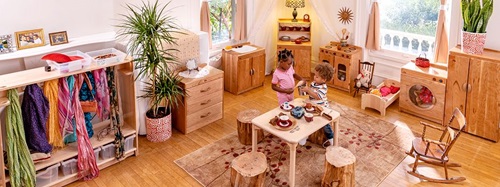 Two children playing with a tea set at a small table in a bright, organized play area.