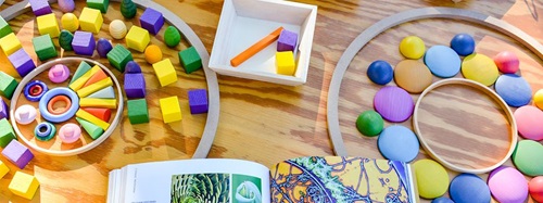 Overhead view of colorful loose parts, including blocks, rings, and flat stones, on a wooden surface.
