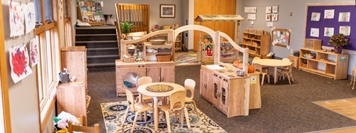 A classroom with wooden play furniture, including a kitchen, laundry, and tables with chairs.