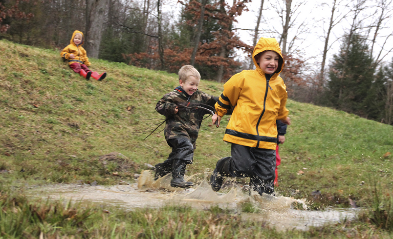 children running down a hill into a large muddy puddle