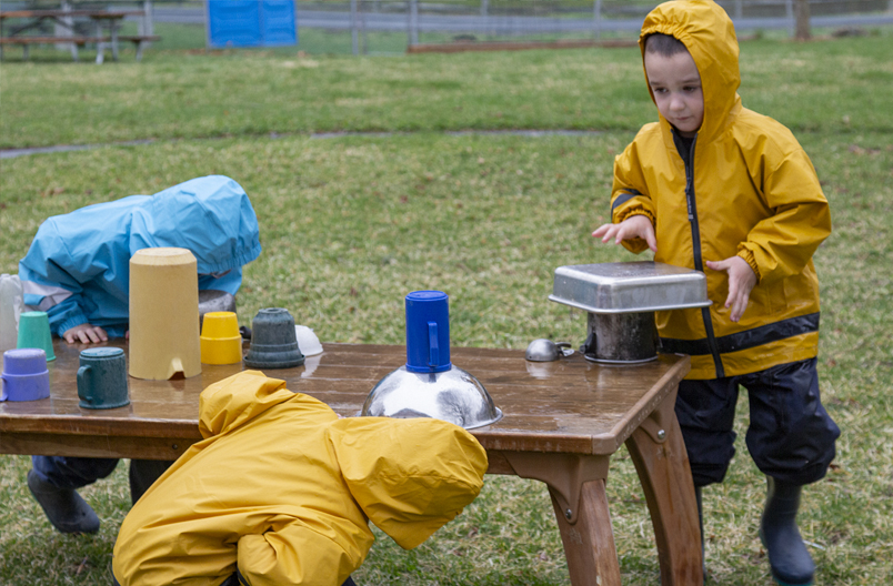 Children setting out loose parts containers to make music in rain.