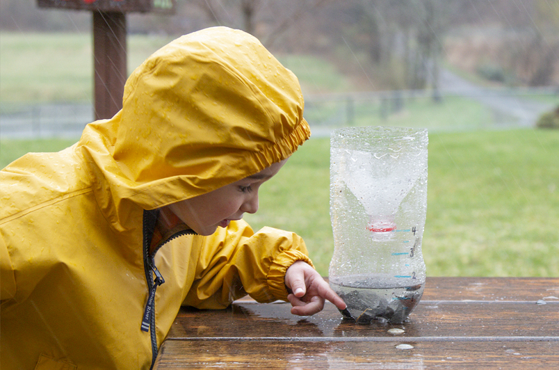 Child in the rain using soda bottle rain gauge
