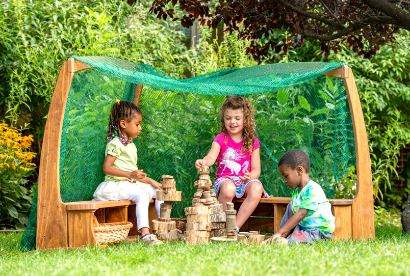 Children playing outside sit under an arbor