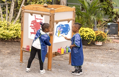 Two children painting on an outdoor easel