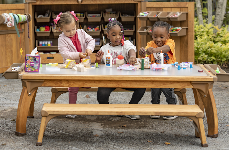 Three children doing a craft project at an outdoor table