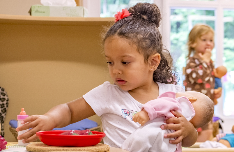 Preschool girl playing with a doll in the dramatic play center