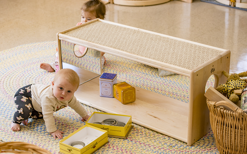 Two children playing with a Community Playthings crawler shelf