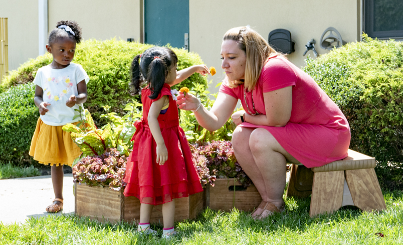 A teacher and child smelling a flower outside