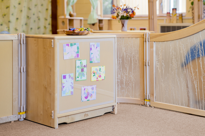 A Community Playthings shelf with children's art displayed on the back of it