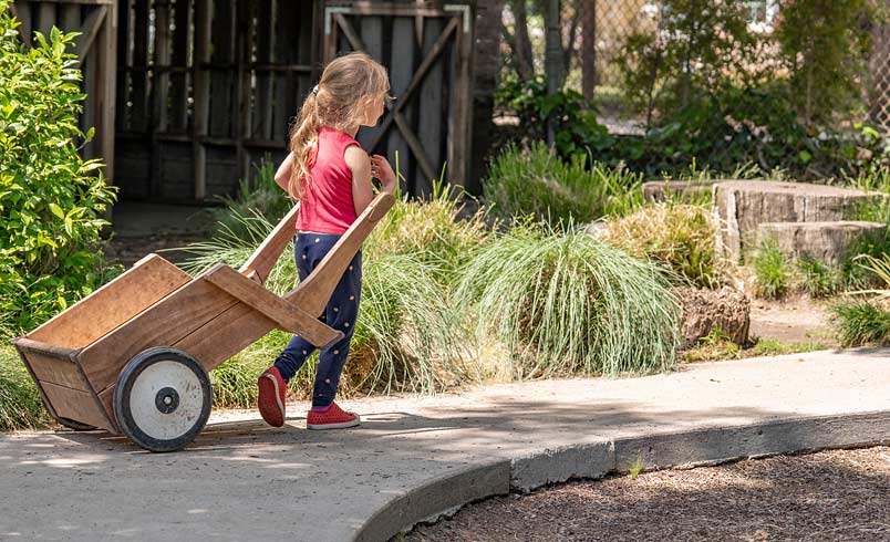 Child pulling Outlast Wheelbarrow along path in outdoor space