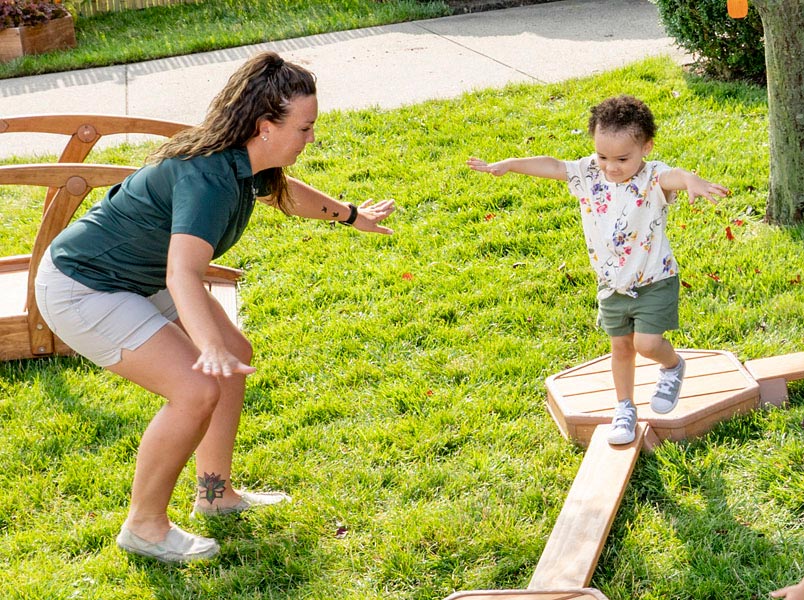 Toddler on Outlast Balance Beam with Teacher assisting