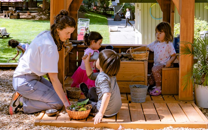 Teacher kneeling in front of Outlast Playhouse, talking with a child