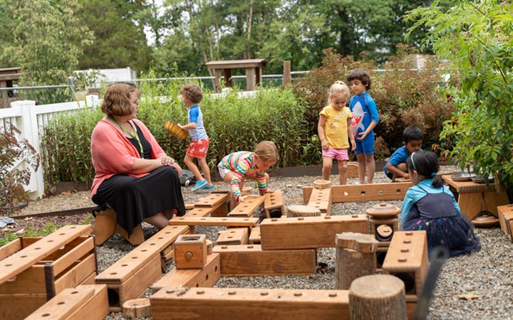 Teacher sitting to the side of play space while several children are deeply engaged in building with Outlast Blocks