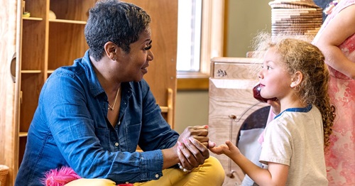 An adult and a child sit facing each other, holding hands and talking.
