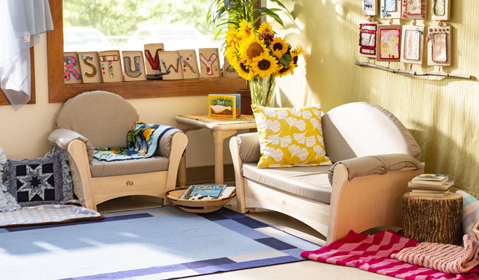 A cozy reading nook with a wooden armchair and loveseat, a small table, and a blue rug.