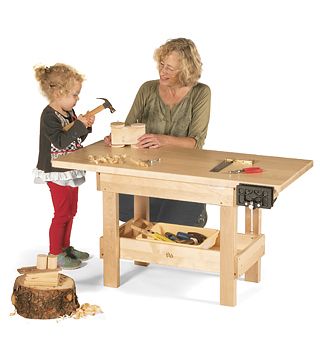 A child is using a workbench with the assistance of a teacher