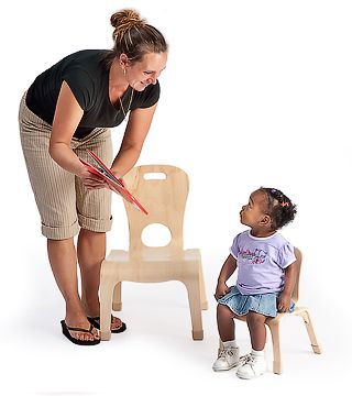 A child on a child-sized chair and a teacher standing next to a Teacher Low Chair