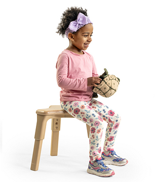 A preschool girl sitting on a stool
