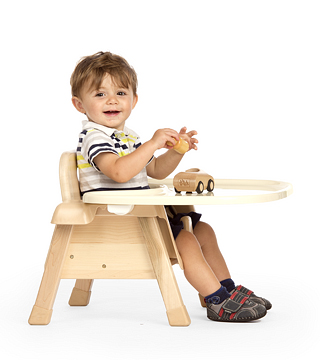 A child sits on a chair with tray and plays with a wooden car