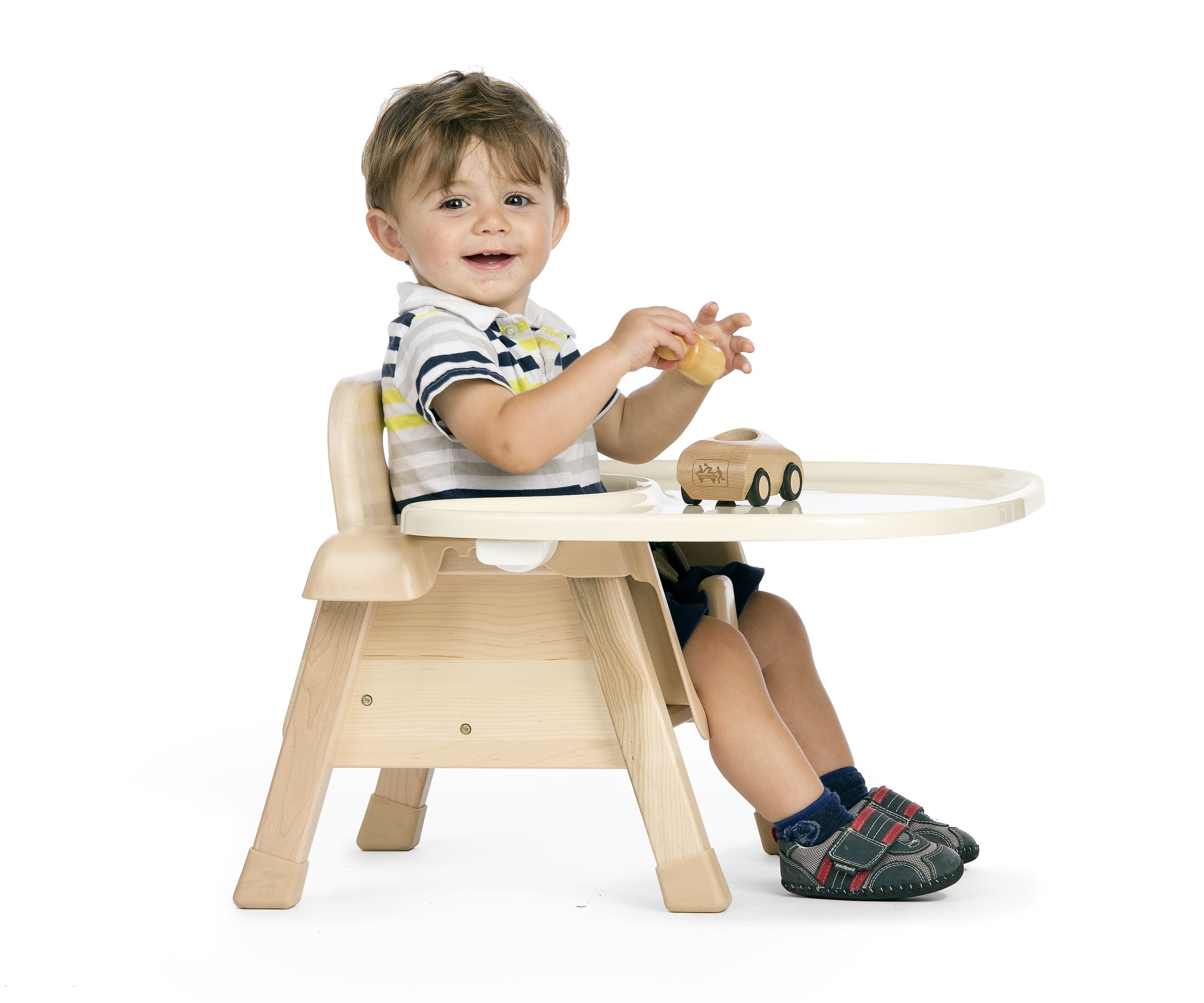 A child sits on a chair with tray and plays with a wooden car
