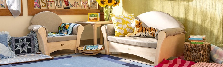 A cozy corner of a child care setting with a children’s sofa, a large toy tiger and a vase with flowers on a wooden table
