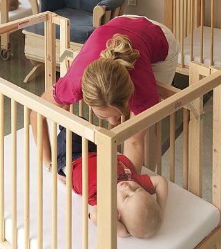 A teacher is lifting a baby out of a BackSafe Crib with lowered side