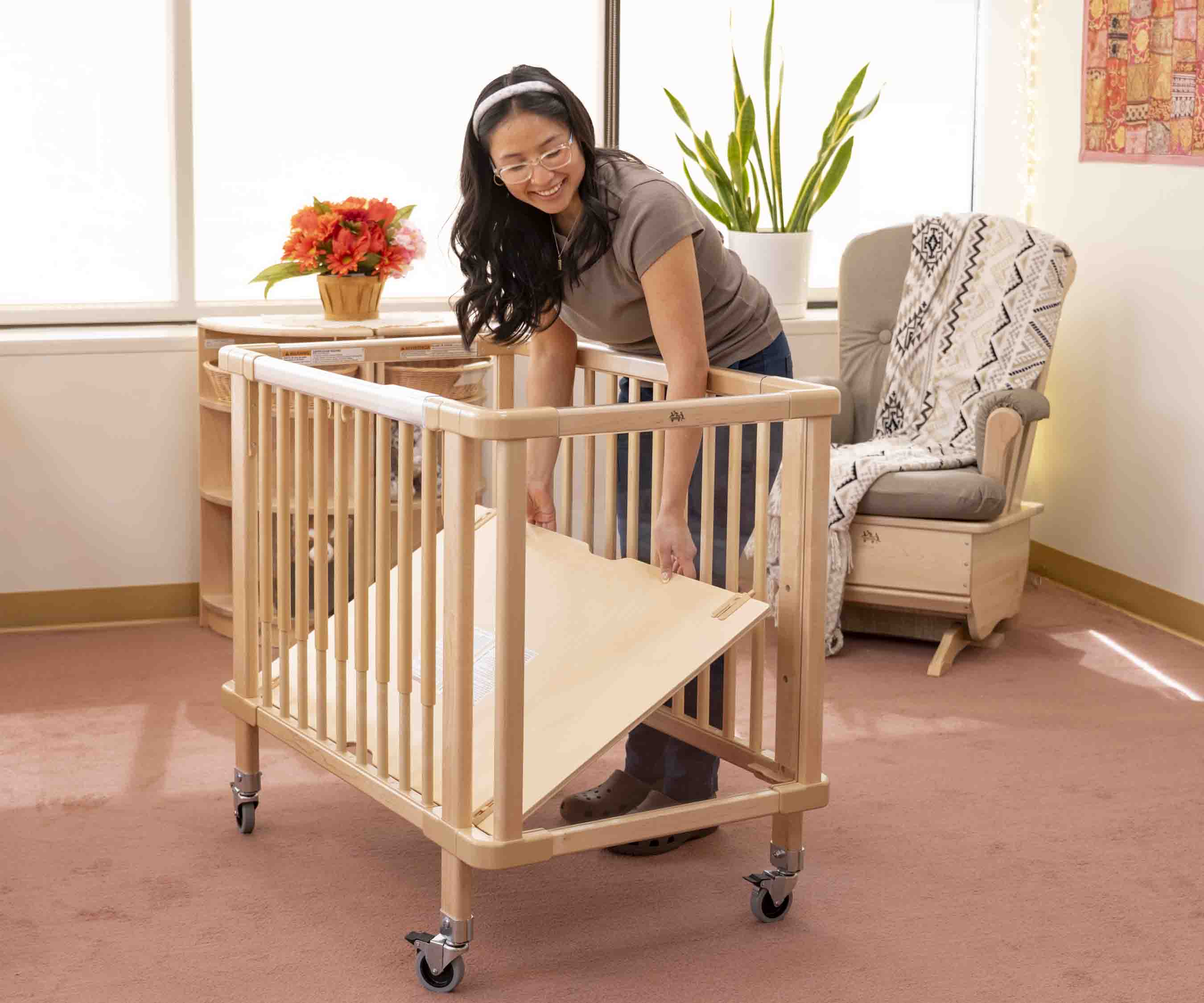 A teacher adjusting the mattress height of a crib.