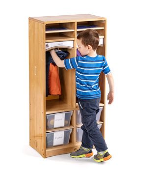 A boy is hanging his jacket into solid maple wood preschool cubbies with totes