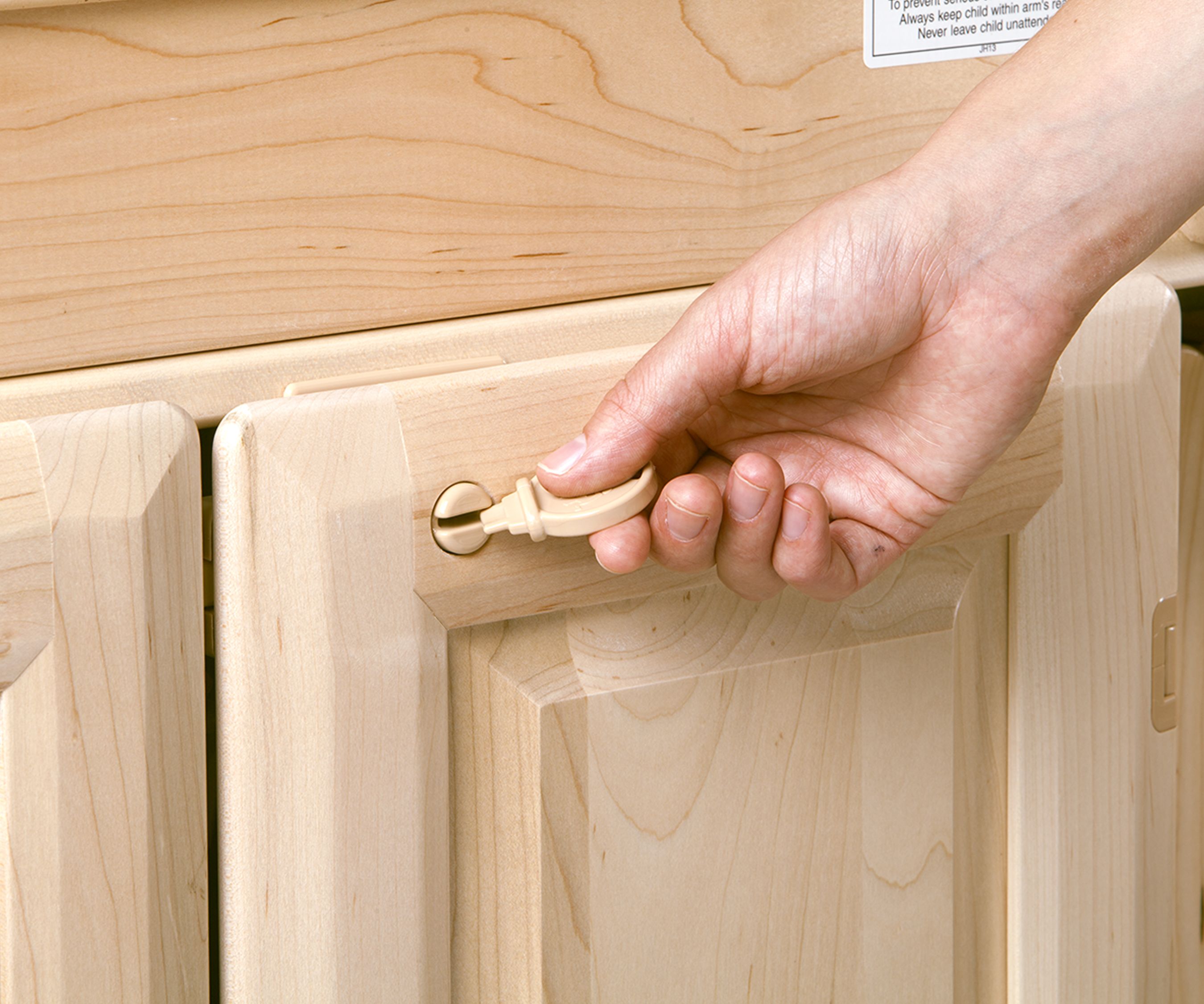 A hand holds a plastic key in front of a cabinet door with locking feature