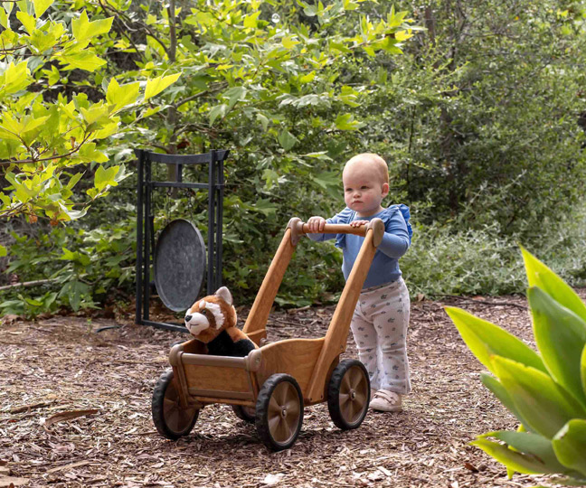 Toddler pushing stuffed animal in Outlast Push Wagon