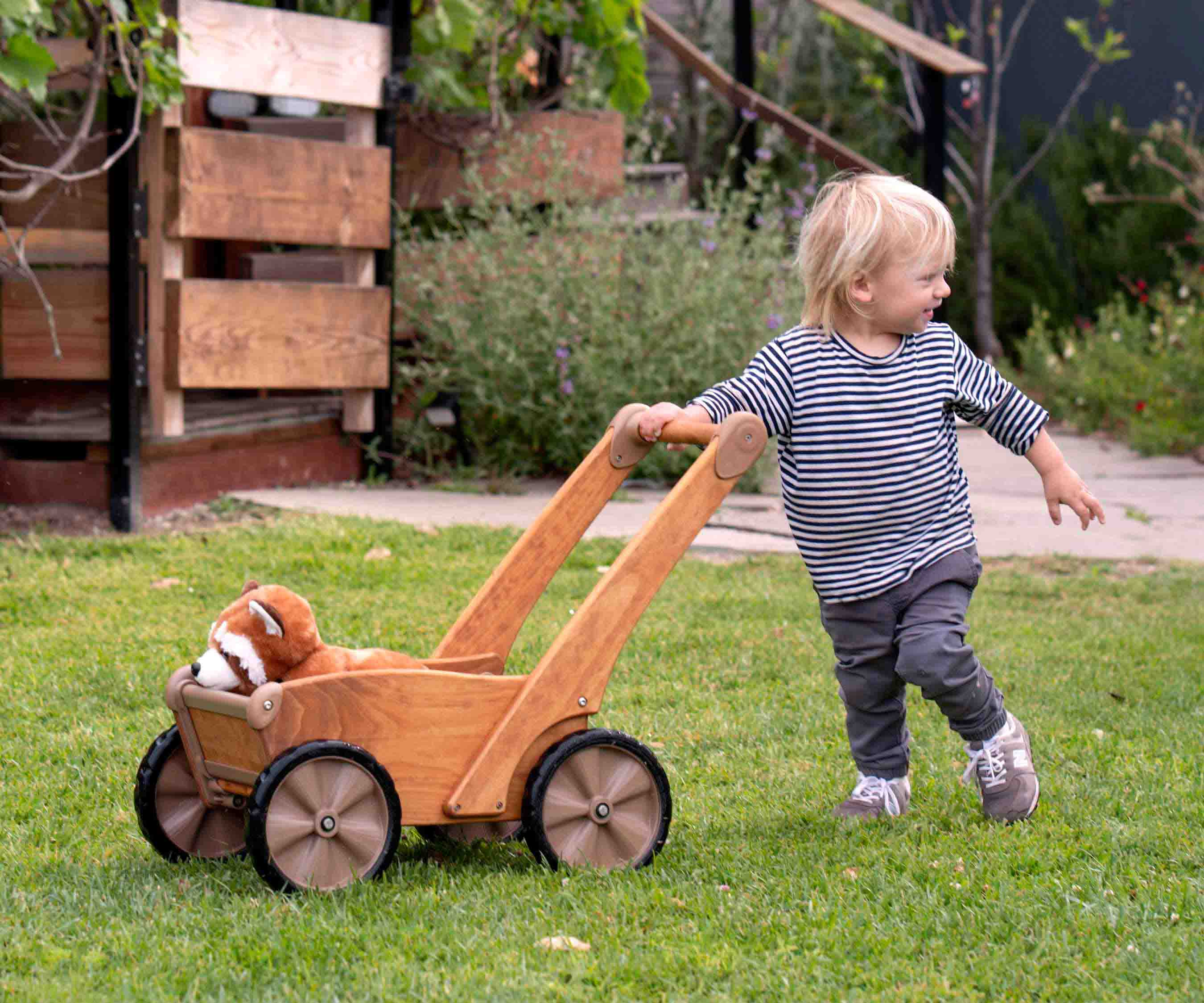 Older toddler pushing a stuffed animal in the Outlast Push Wagon