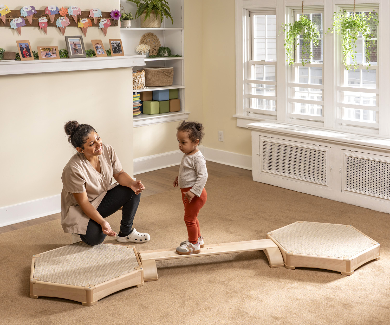 a teacher watching a toddler walk on a balancing beam